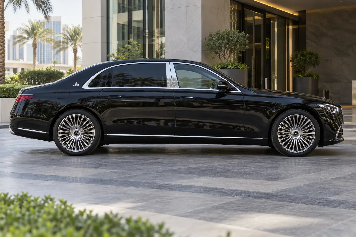 Black Mercedes-Maybach S-Class chauffeur sedan in side profile outside a Dubai executive entrance, with all doors closed